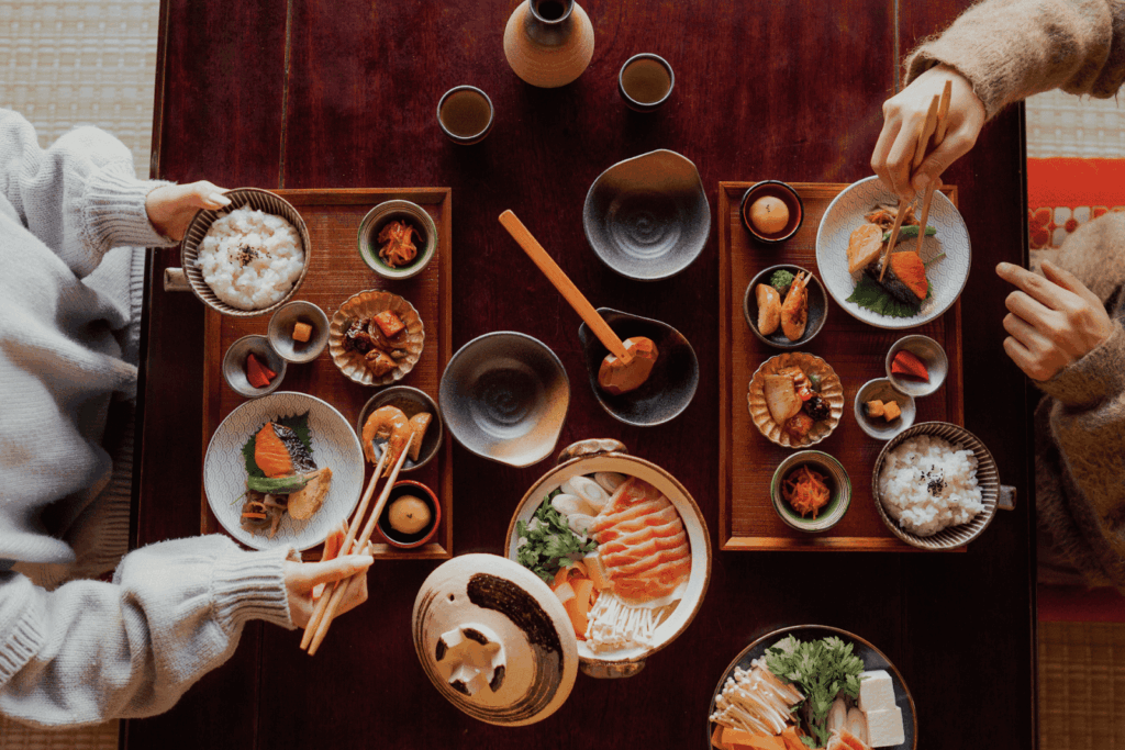 Top view of two people eating a traditional Japanese meal with various small dishes.
