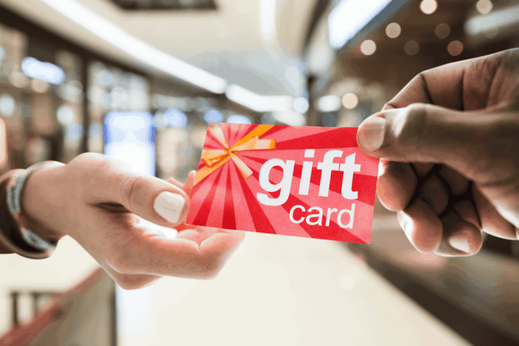Two hands exchanging a red gift card in a shopping mall.