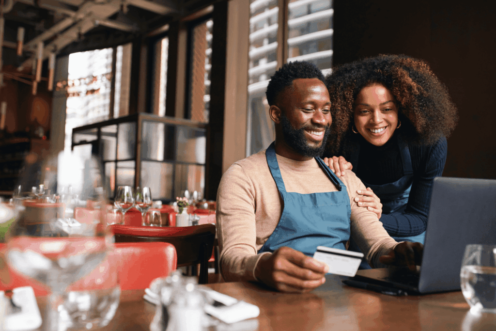 Two restaurant workers smiling while using a laptop and holding a credit card.