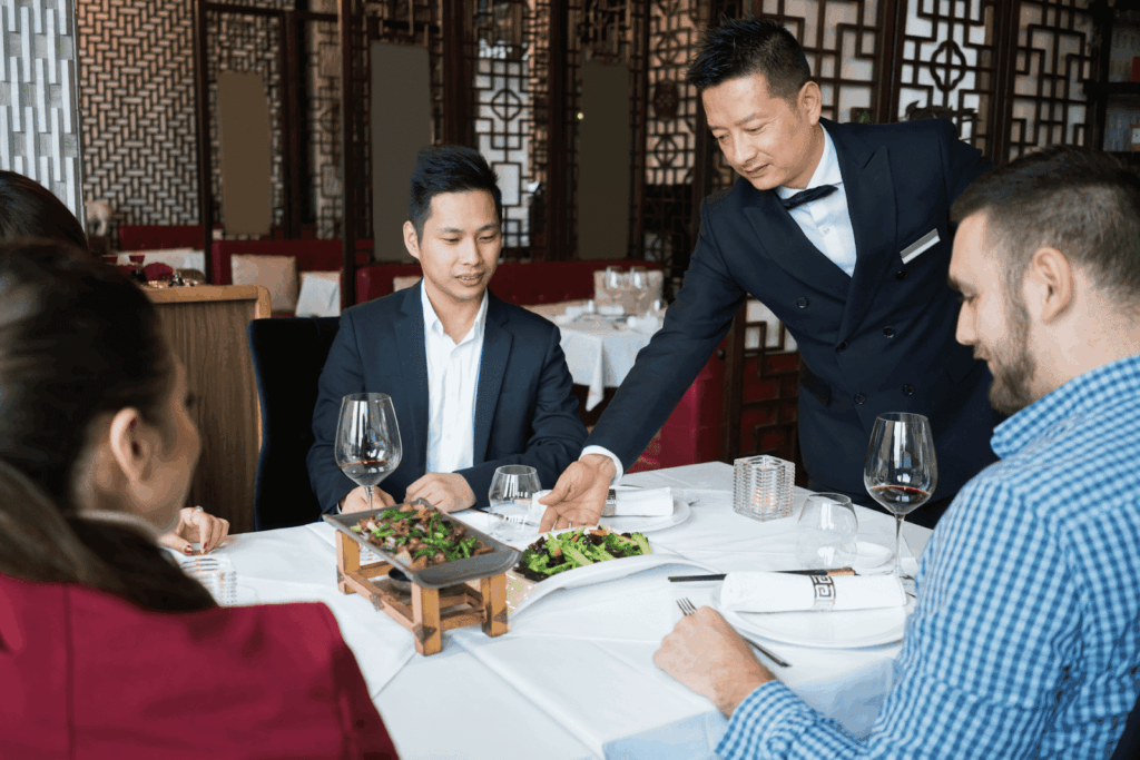 Waiter serving food to a group of people dining at a formal restaurant table.