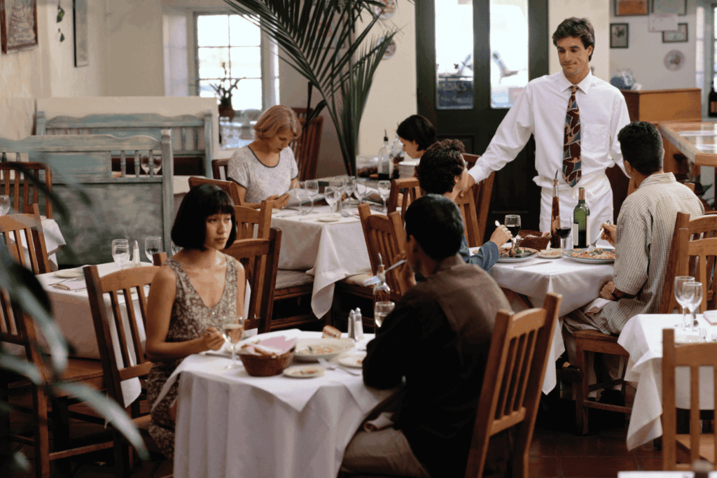Waiter speaking with diners at a busy restaurant with tables set for service.