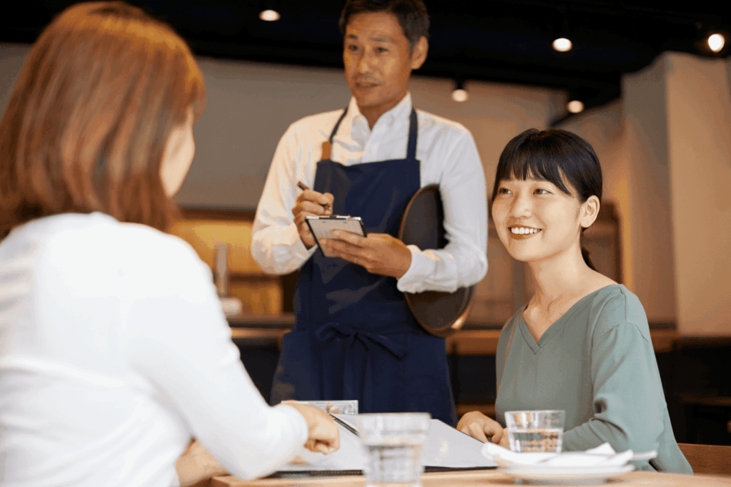 Waiter taking an order from two women seated at a restaurant table, one smiling