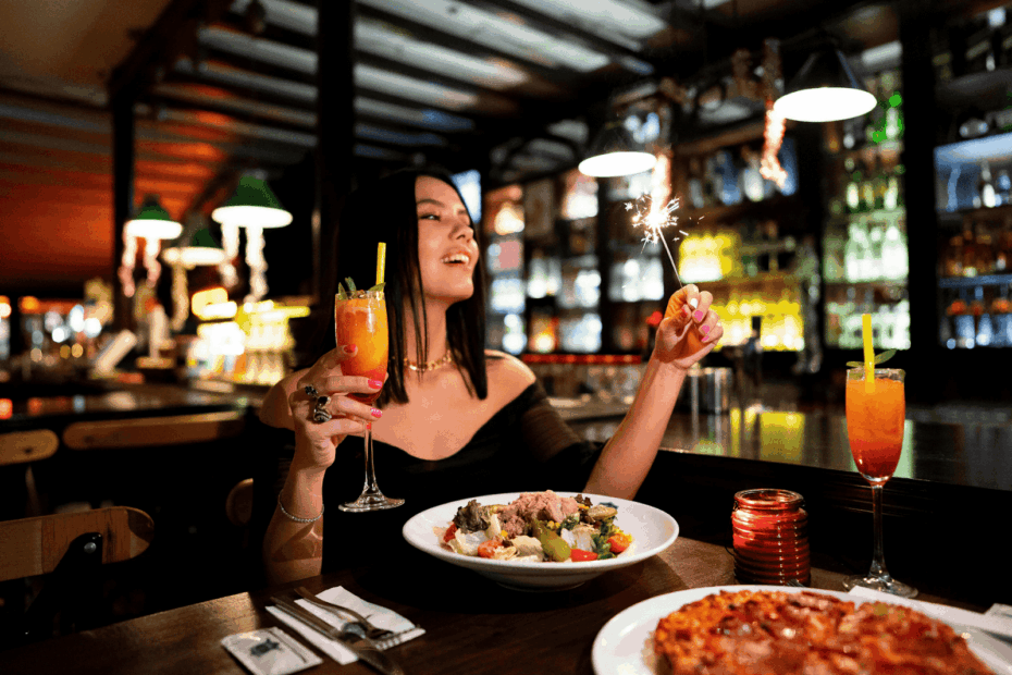 Woman celebrating at a restaurant with a cocktail in one hand and a sparkler in the other.